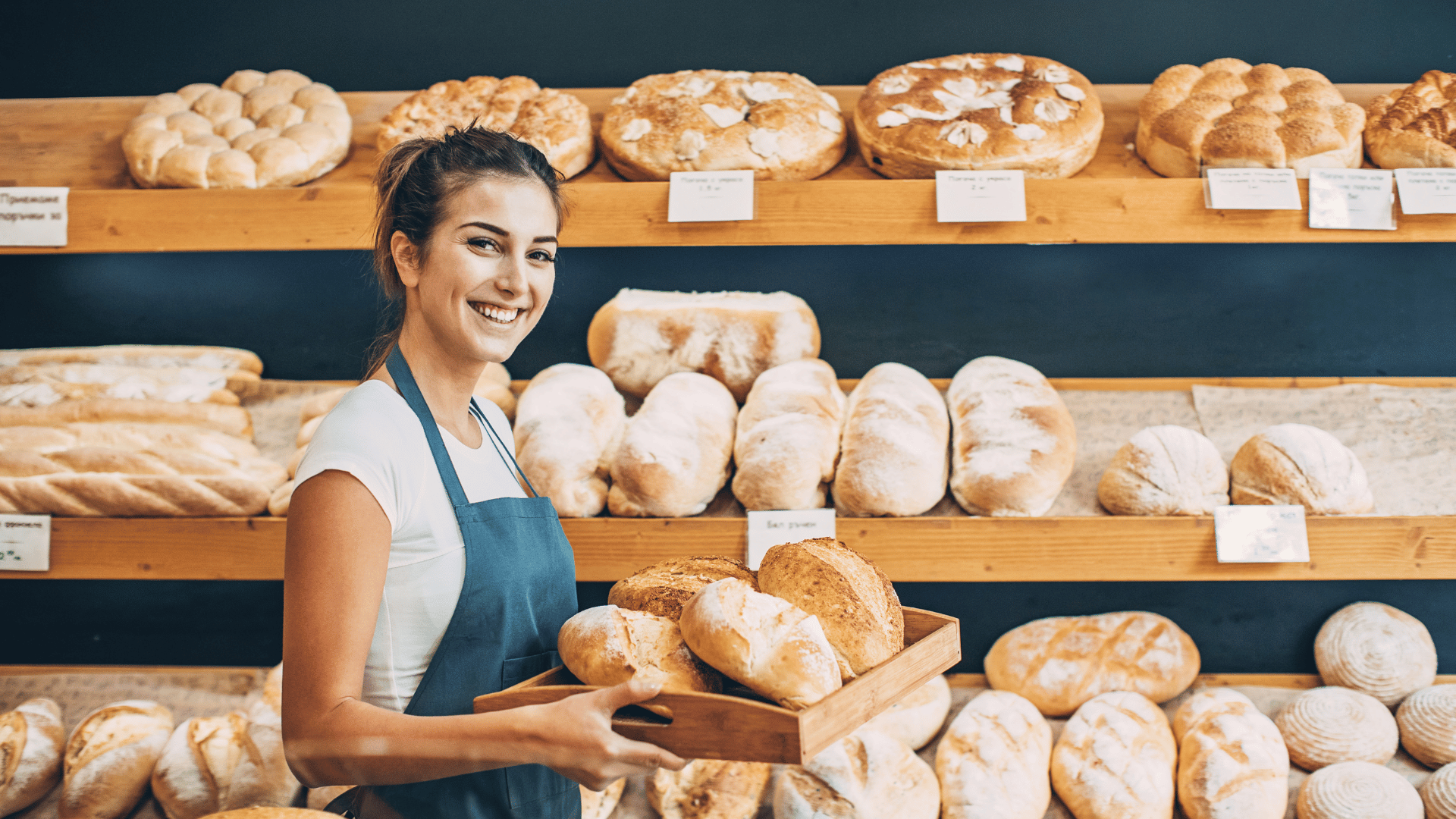 Mulher sorridente em padaria segurando bandeja com pães artesanais, representando empreendedorismo e microcrédito para pequenos negócios